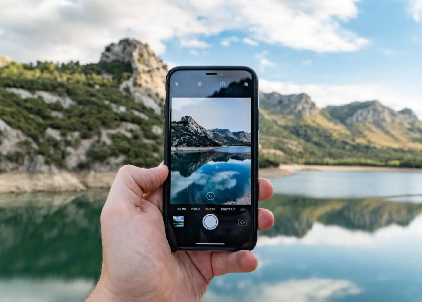 someone holding a phone with the camera open in front of a mountainous landscape