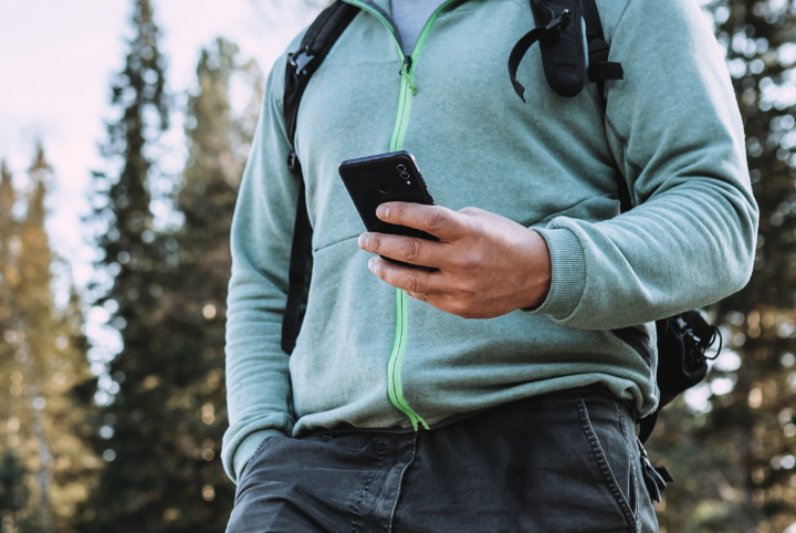 a man look at his phone while he stands in a forest