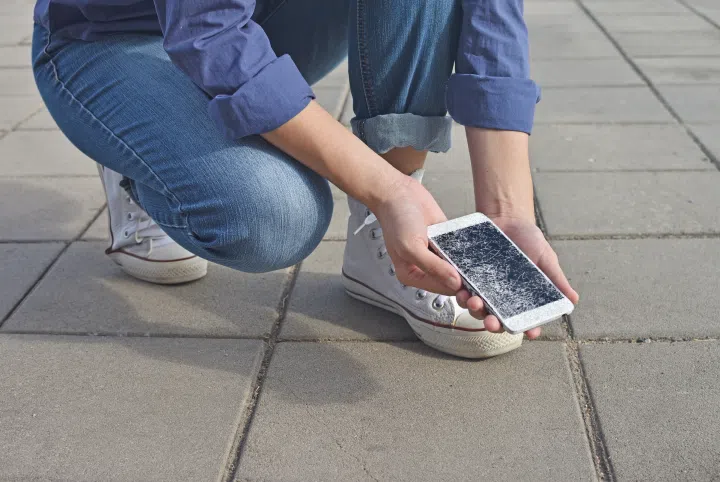 person kneeling next to a broken phone and picking it up