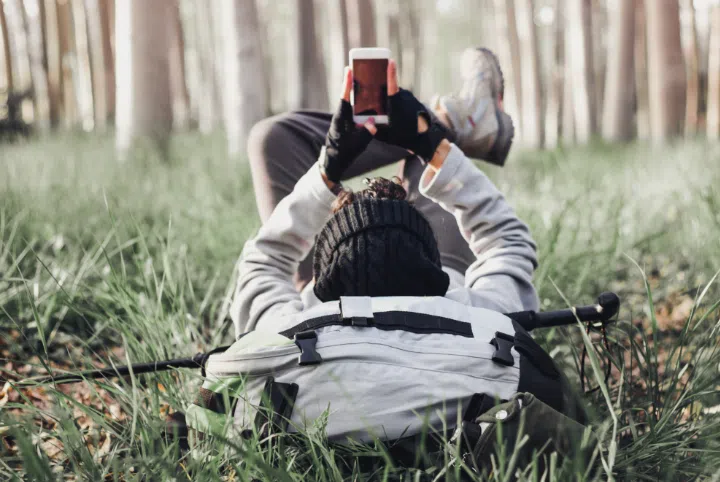 person laying in the grass in forest looking up at his phone