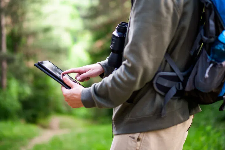 a person holding a tablet while standing in a forest