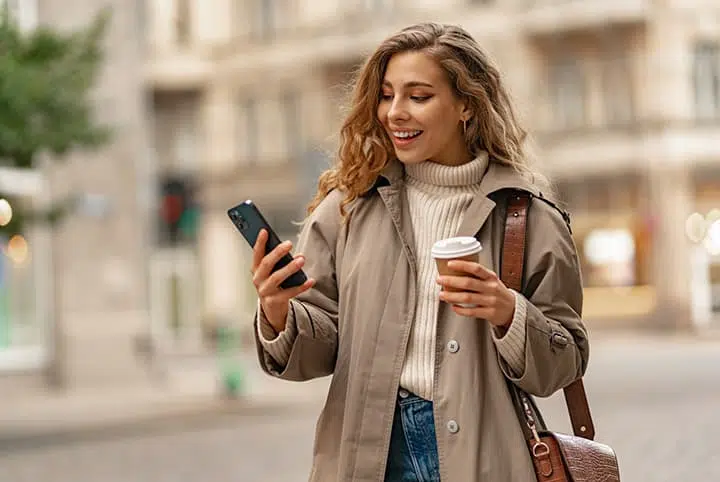 a young lady holding a phone and a coffee walking around town