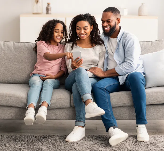 a family sitting on the couch looking at a phone