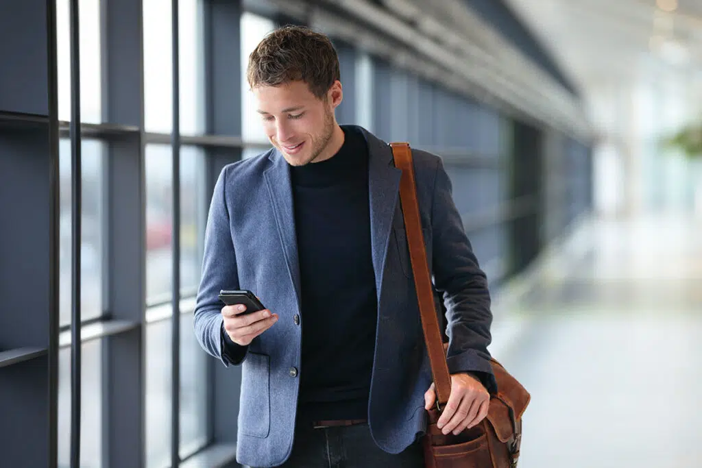 A person dressed in business attire walking through a hallway looking at their phone
