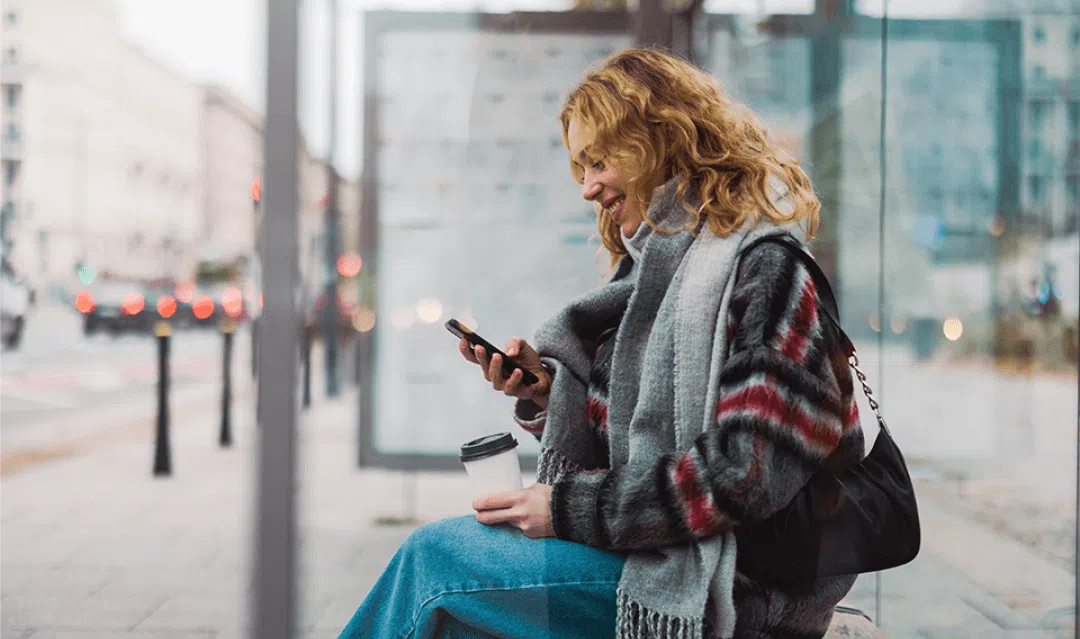 lady sitting at a bus stop with her phone out