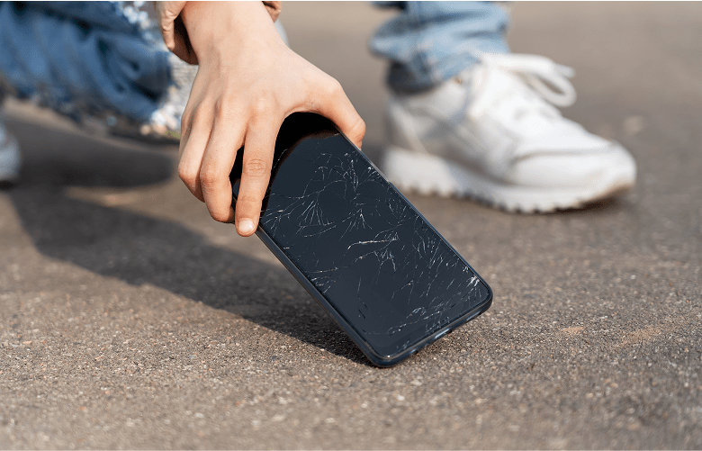 A person picking a phone up off the ground, the screen is cracked