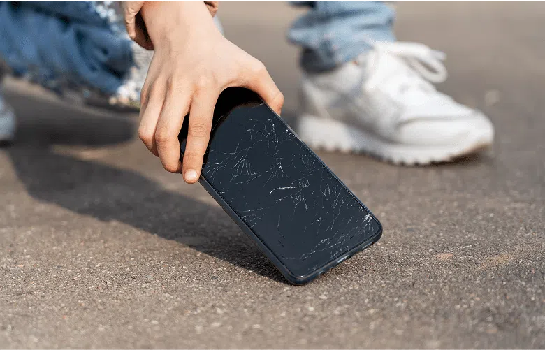 A person picking a phone up off the ground, the screen is cracked