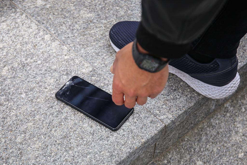 Person picking up a phone with a cracked screen off the ground