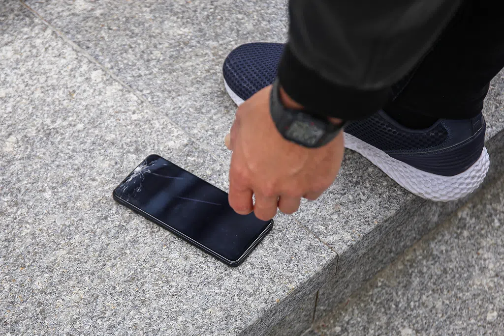 Person picking up a phone with a cracked screen off the ground