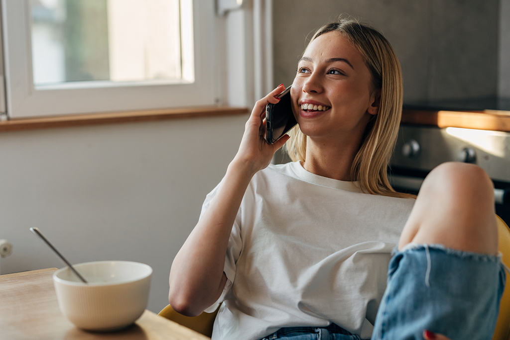 Woman sitting down at a table talking on the phone with an empty bowl in front of her